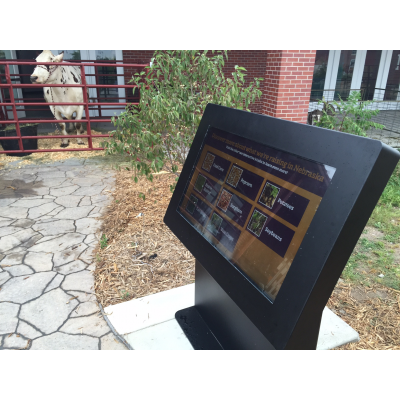 An outdoor touch screen kiosk with a cow in the background